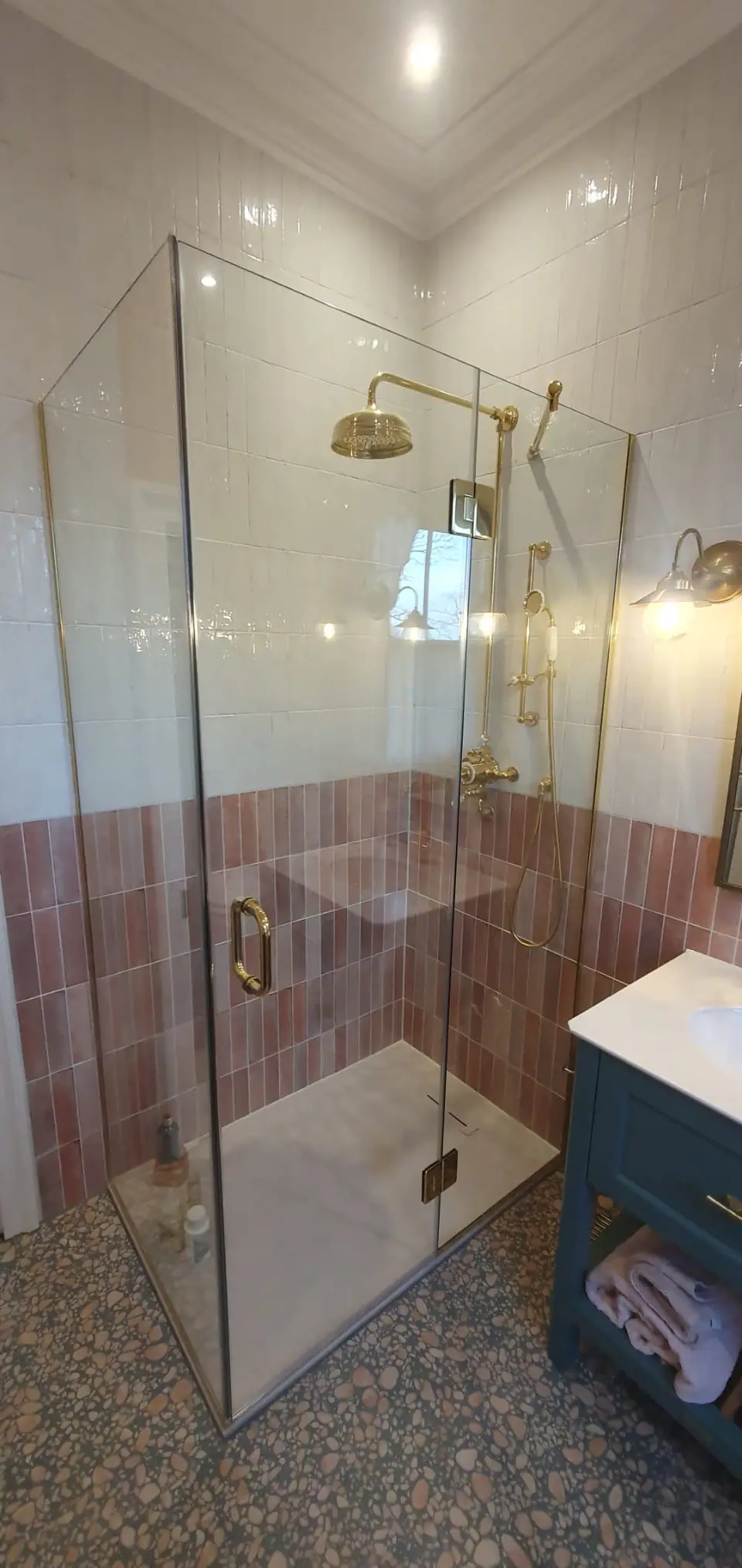 Glass shower enclosure with brass fittings and two-tone pink and white tiles
